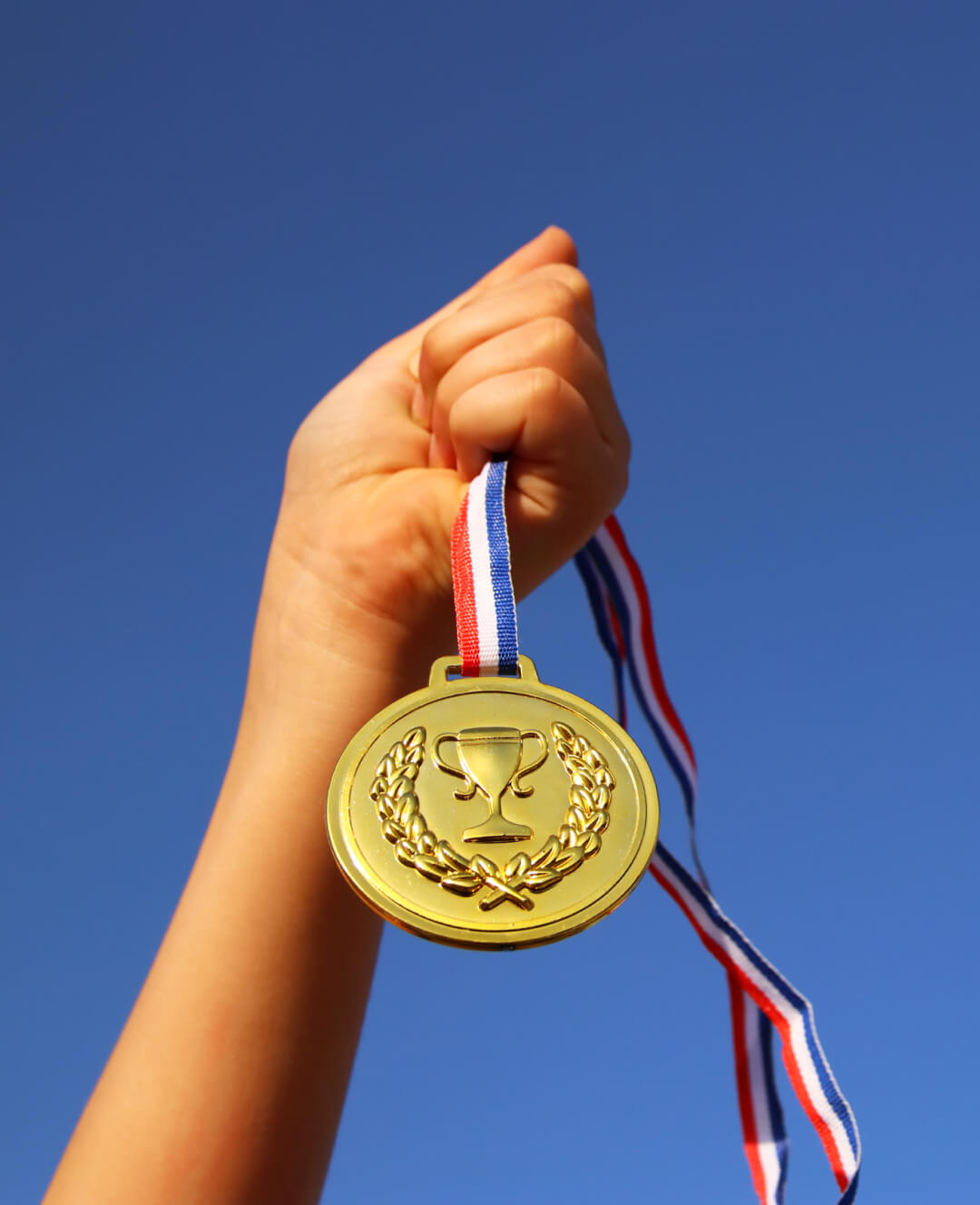 A person holding a gold medal against a blue sky.